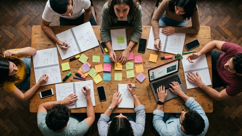 Overhead shot showing teamwork with people sat around a table, brainstorming ideas and making notes