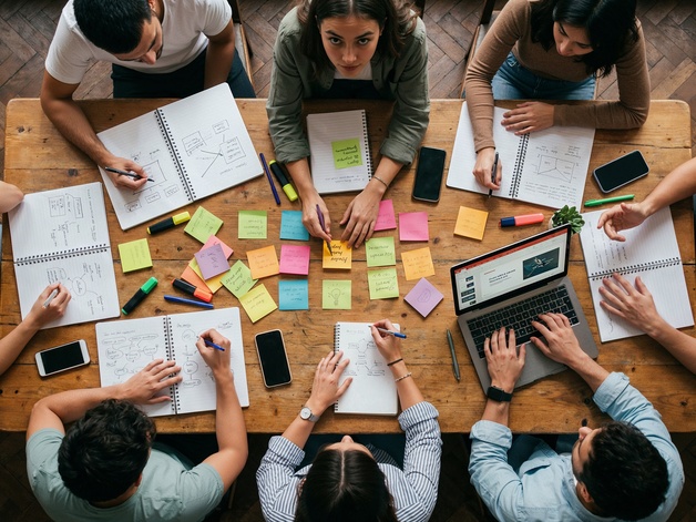 Overhead shot showing teamwork with people sat around a table, brainstorming ideas and making notes